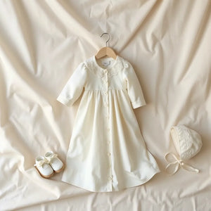 Elegant christening gown with lace trim, matching bonnet and booties on a cream satin backdrop